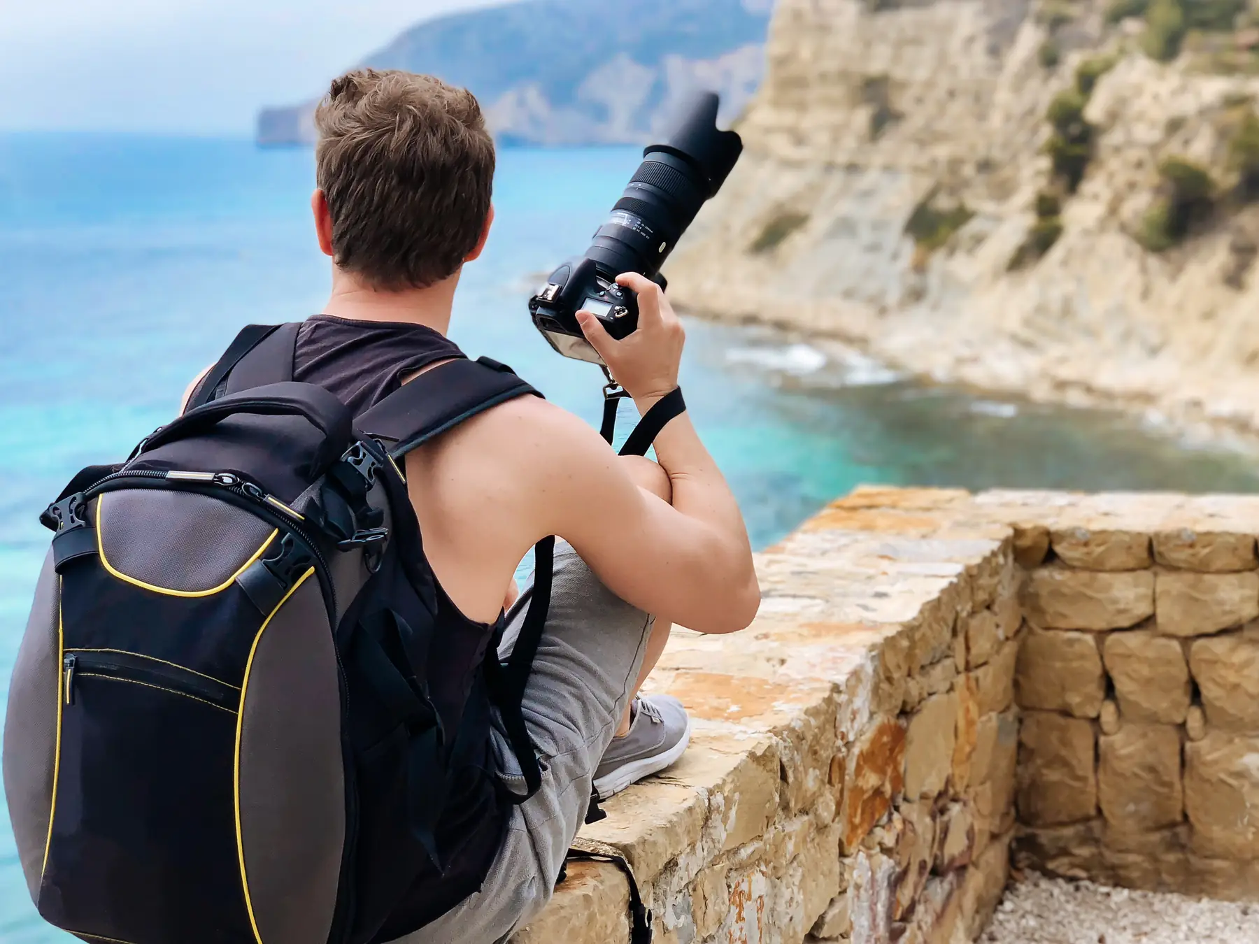 A photographer with a backpack framing a shot of a rocky coastline