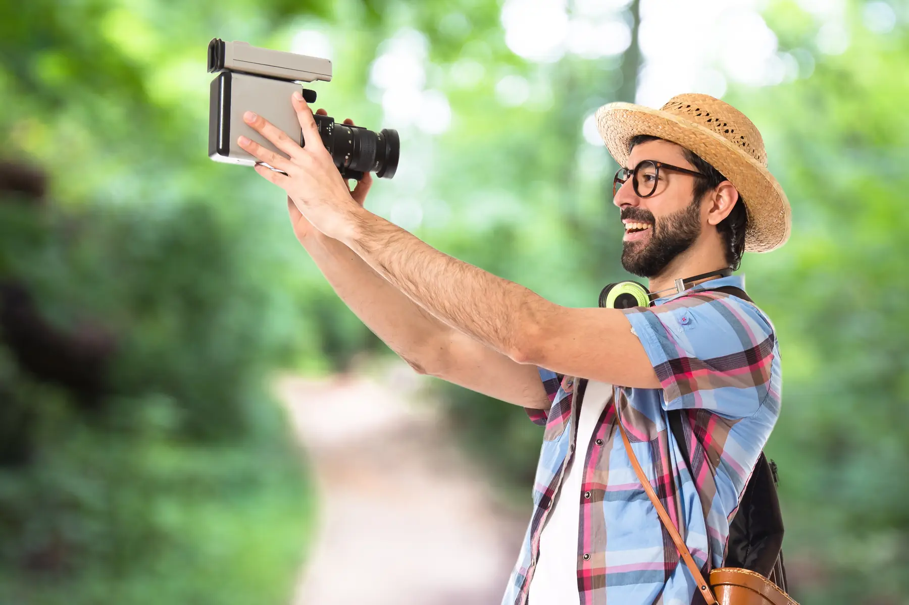A traveller in a straw hat filming with a handheld camera on a forest path